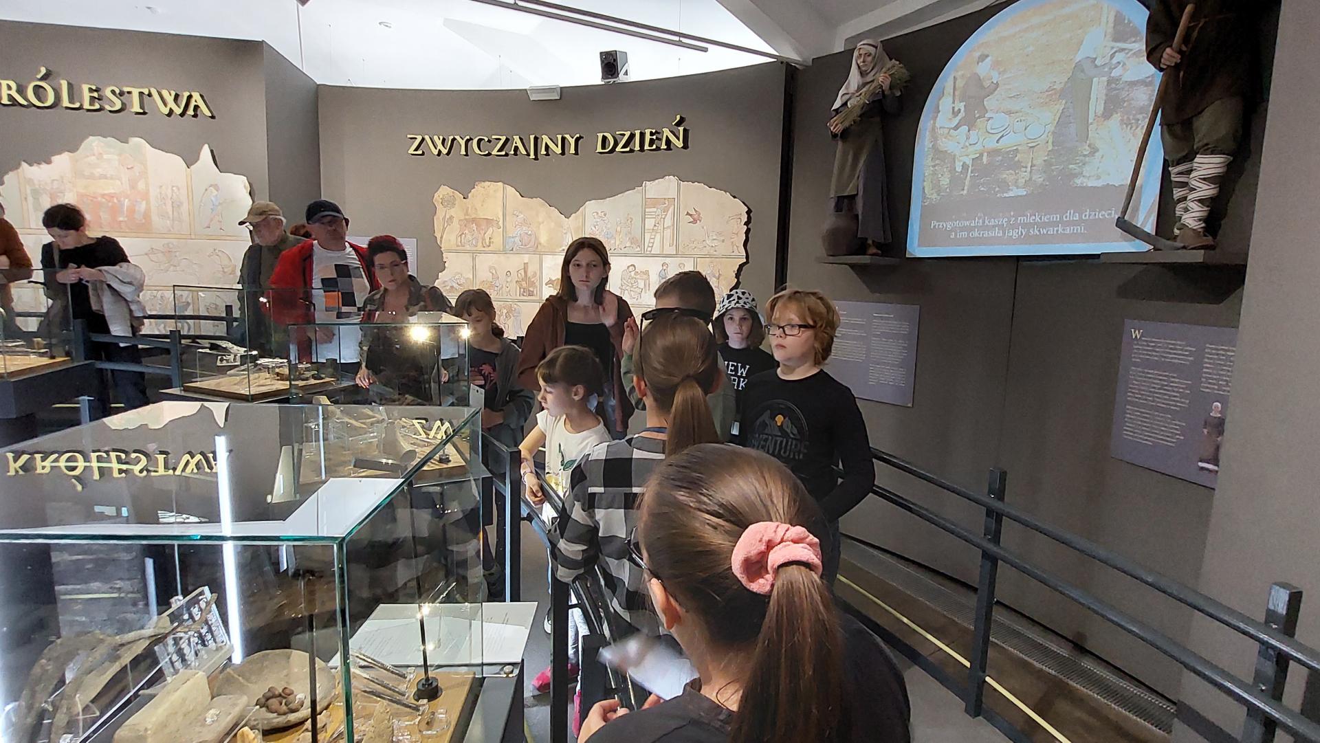 dzieci ogladaja ekspozycje muzealną z gablotami