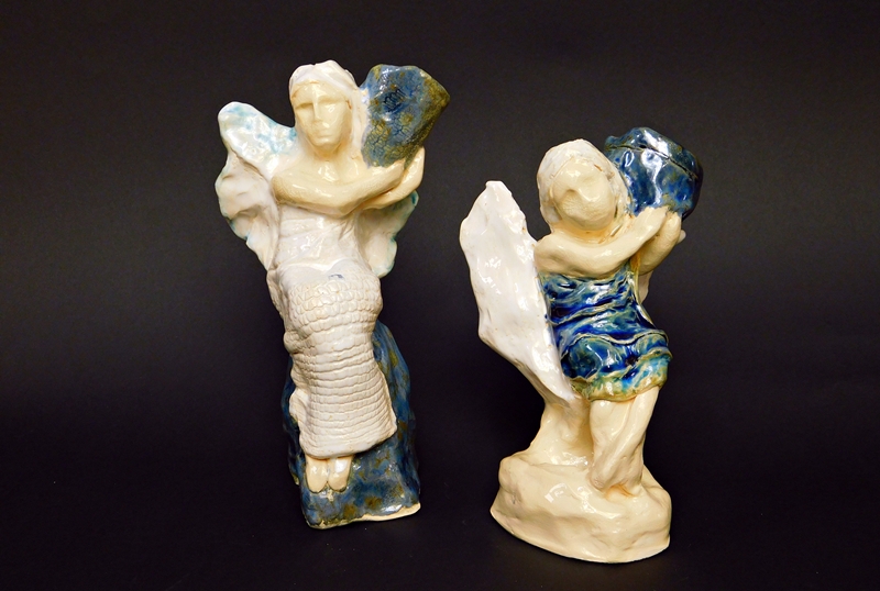 dwie figurki ceramicznych aniołów trzymających przy głowach wazy