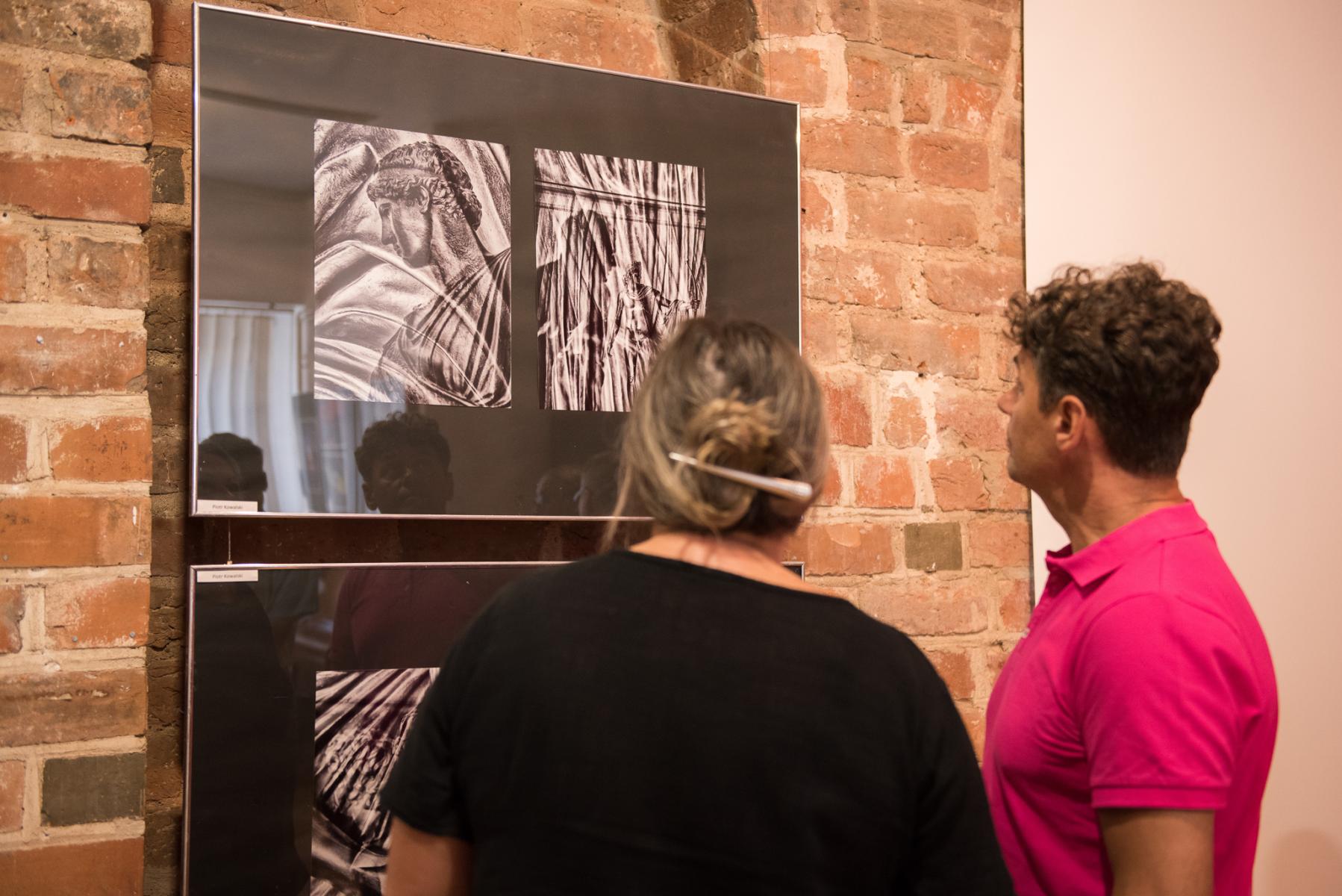 dwoje ludzi ogląda fotografie zawieszone na ścianie